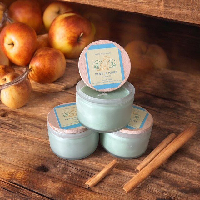 Three pastel green jars of cream with cinnamon sticks and apples.