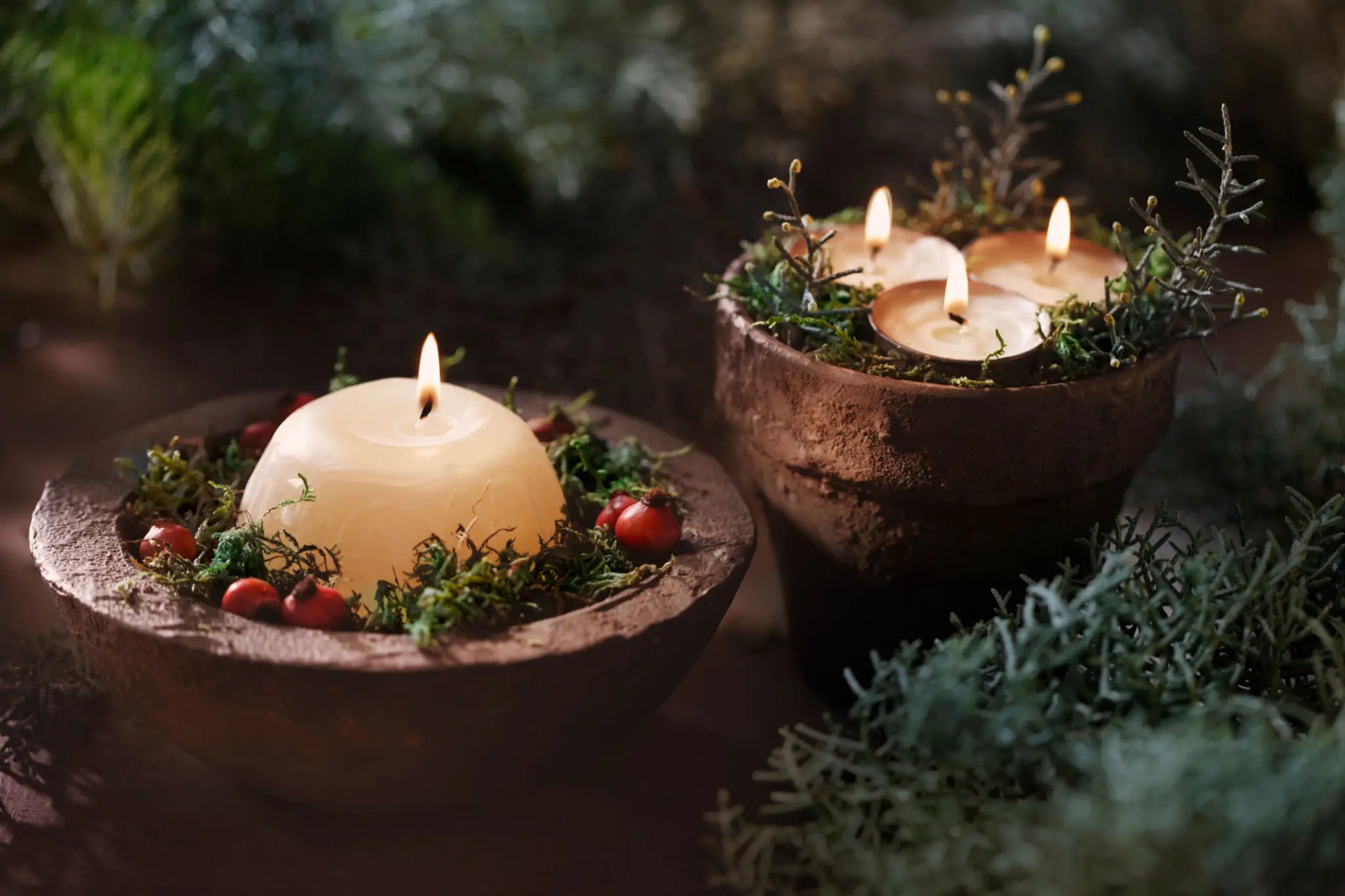 Two rustic candles in wooden holders surrounded by greenery and berries.