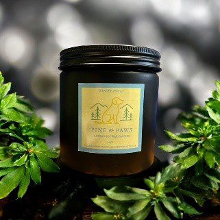 Amber glass candle jar with a yellow label among green plants.