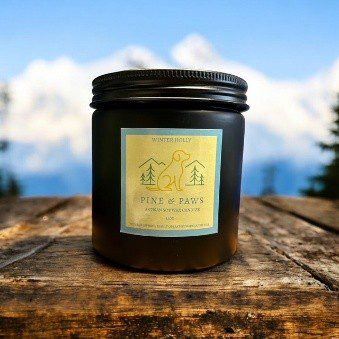 A black jar candle with a gold label on a wooden surface outdoors.